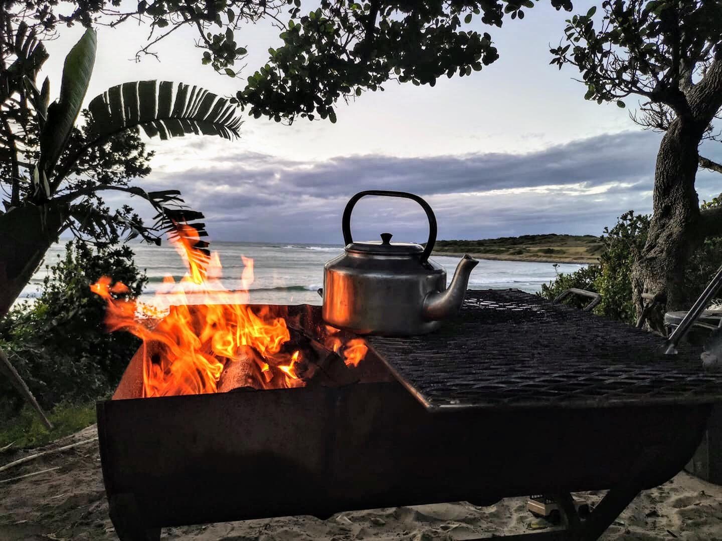 A braai fire and kettle with the sea in the background at dusk