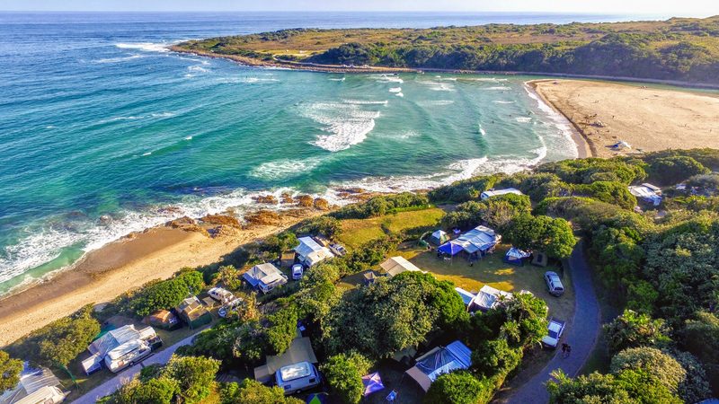 Aerial view over Yellow Sands Caravan Park, campsites lining the beach at the Kwelera River mouth